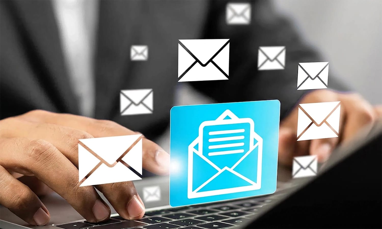 Person tippt auf Laptop. Davor leuchten Mail-Icons.