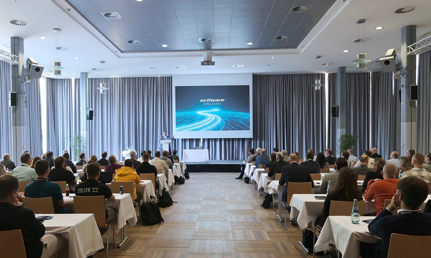 In einem Saal sitzen viele Menschen und warten auf den anstehenden Vortrag.