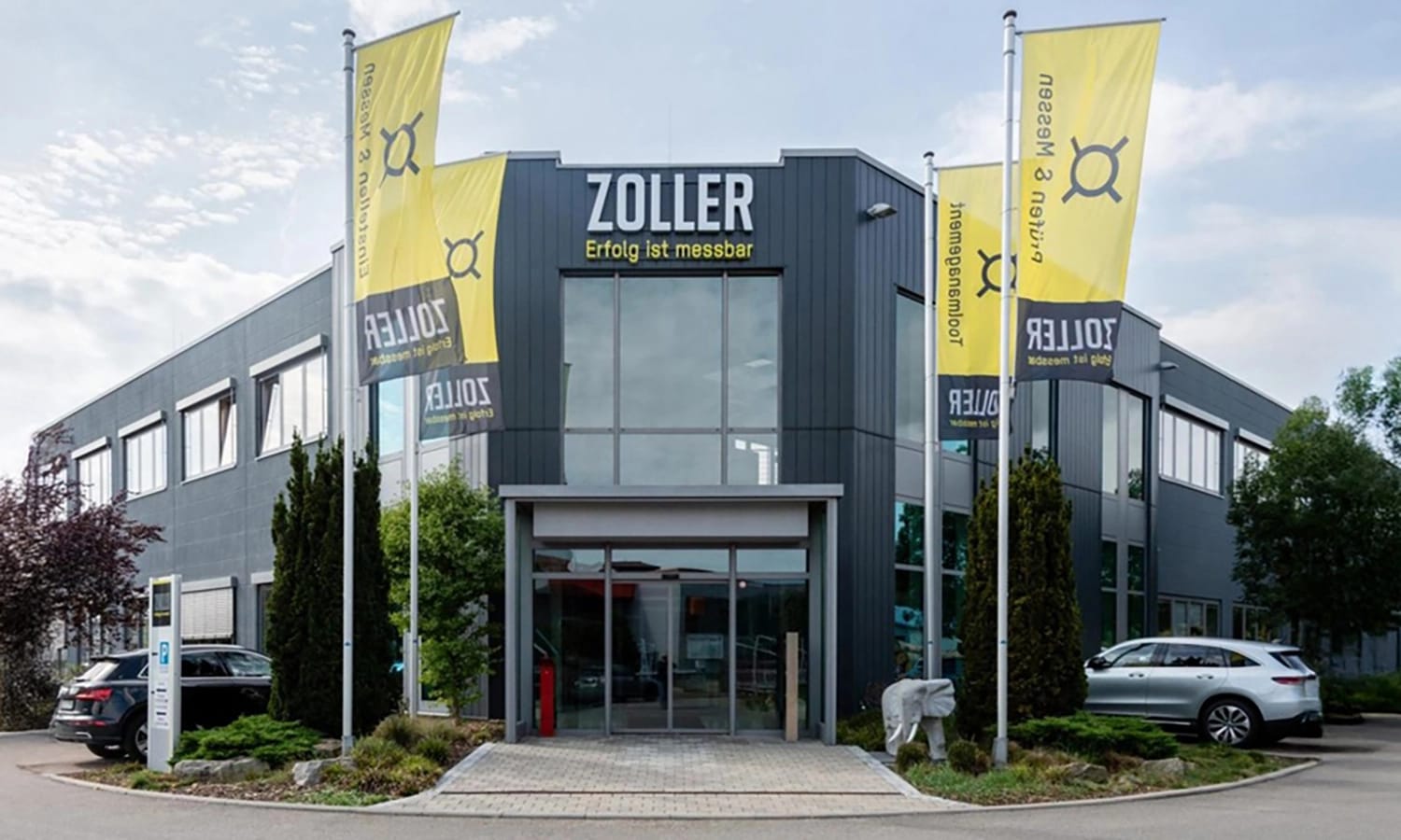 Firmengebäude von e‑zoller mit Fahnen und Eingang – moderner Unternehmenssitz für Präzisionsmesstechnik und digitale Werkzeugverwaltung.